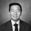 Black and white headshot of a smiling East Asian man in a suit and tie.