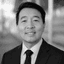 Black and white headshot of a smiling Asian man in a suit and tie.