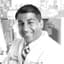 Smiling doctor in a lab coat and striped tie in a clinical setting.